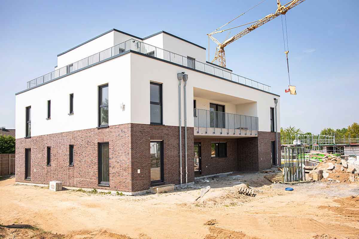 Neubau in Bonn Beuel mit weißer Putzfassade und Klinkersockel, dahinter ein Baukran
