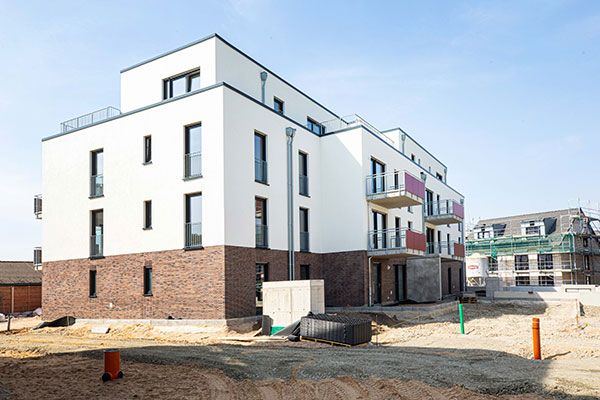 Mehrgeschossiger Neubau mit weiß verputzter Fassade und Klinkersockel vor blauem Himmel